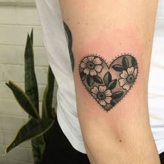 a heart shaped tattoo with flowers on the arm