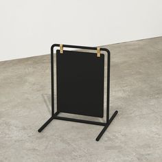 a black and gold easel sitting on top of a cement floor next to a white wall