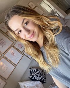 a woman with long blonde hair standing in front of a wall full of framed pictures