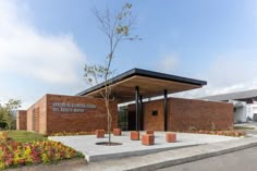 a brick building with a tree in the front and flower beds around it on either side