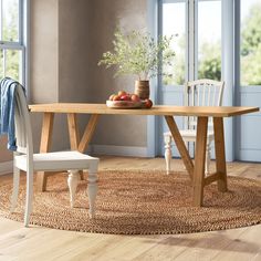 a wooden table sitting on top of a rug next to a white chair and potted plant