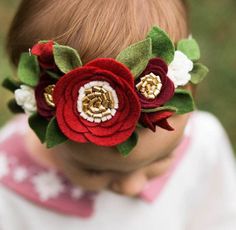 a baby wearing a red flower headband with green leaves and white flowers on it