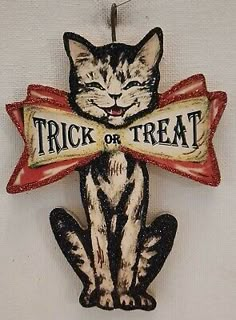 a black and white cat holding a trick or treat sign hanging from a hook on a wall