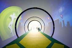 a tunnel with people walking through it on a green carpeted floor and white walls