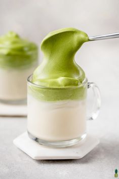 two glasses filled with green and white desserts on top of each other, one being whipped cream