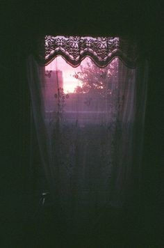 the sun is setting through the window in the dark room with sheer curtains on the windowsill