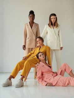 three women standing and sitting next to each other in front of a white wall, with one woman laying on the floor