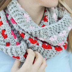 a woman wearing a gray and red crocheted scarf with hearts on the edge