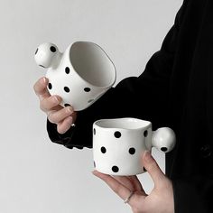 a woman holding two white coffee mugs with black polka dots on them, both in their hands