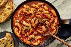 a skillet filled with pasta and shrimp on top of a marble table next to bread