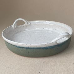 a white and blue dish with handles on a beige tableclothed surface, ready to be used as a serving platter