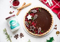 a chocolate tart topped with christmas decorations on top of a white plate next to cookies