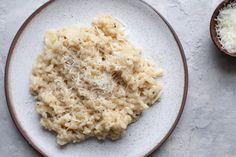 a white plate topped with macaroni and cheese next to a bowl of grated parmesan cheese