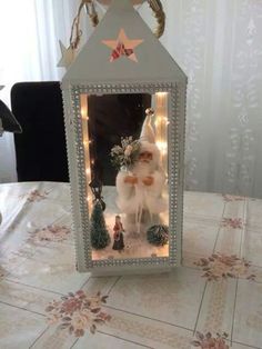 a small white christmas decoration with lights on it's sides and a santa clause in the center