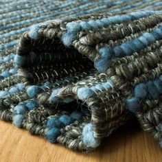 a close up view of a blue and gray rug on a wooden floor, with the end section partially covered by yarn