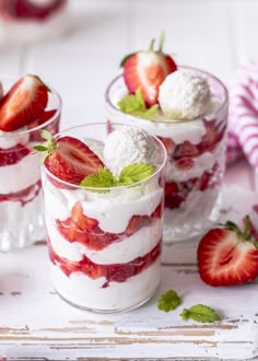 three desserts with strawberries and ice cream in them on a white wooden table