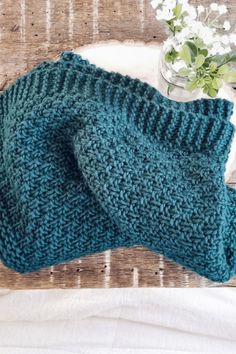 a blue knitted dishcloth on a table next to a vase with white flowers