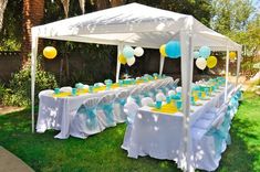 an outdoor party setup with white and blue tables, yellow and white decorations and balloons