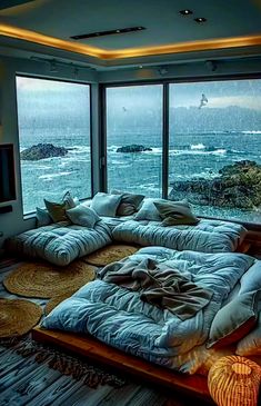 a large bed sitting inside of a living room next to a tall glass window overlooking the ocean