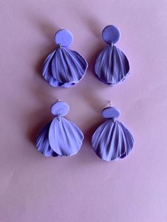 three pairs of purple seashell earrings on a pink background, one is shaped like a shell