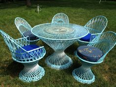 an outdoor table with four chairs and a blue cushion on the grass in front of it