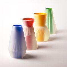 three different colored vases sitting next to each other on a white surface with no one around them