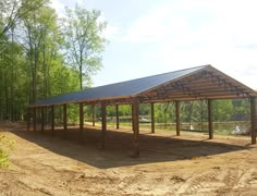 a large metal structure sitting in the middle of a dirt field next to some trees