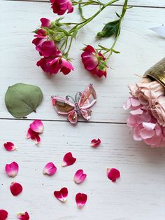 some pink flowers and a butterfly on a white wooden surface with petals scattered around it