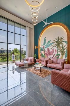 a living room filled with pink couches next to a large glass wall covered in greenery