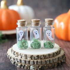 three glass bottles filled with fake grass and ghost faces on top of a tree stump