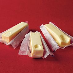 three pieces of cheese sitting on top of wax paper in front of a red background