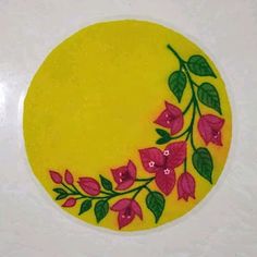 a yellow plate with pink flowers on it and green leaves around the edge, sitting on a white surface