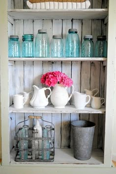 a shelf filled with vases and pitchers on top of wooden shelves next to jars