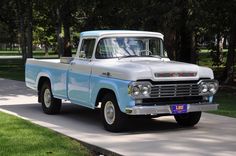 an old blue and white truck parked on the side of a road in front of some trees