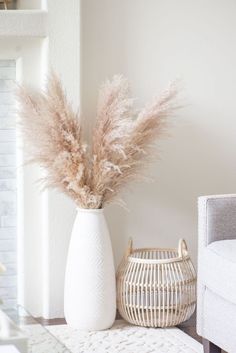 a white vase with dry grass in it next to a chair and rug on the floor