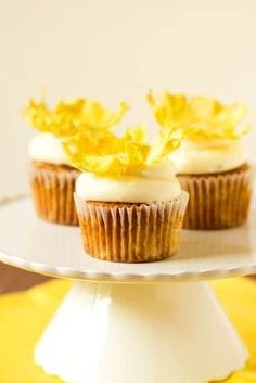 three cupcakes with white frosting and yellow flowers on top sitting on a cake plate