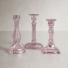 three glass candlesticks are sitting on a white counter top, one is pink and the other is silver