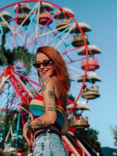 a woman with red hair and tattoos standing in front of a ferris wheel at an amusement park