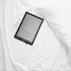 an electronic device laying on top of a white bed with eyeglasses next to it