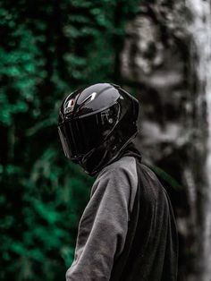 a man wearing a black helmet standing in front of a waterfall with his back to the camera