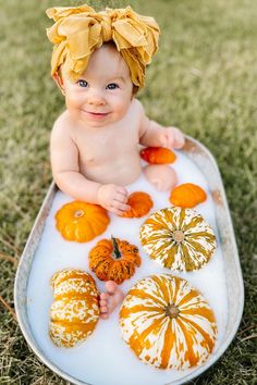 a baby sitting in a bathtub with pumpkins and gourds on it