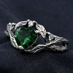 a green heart shaped ring sitting on top of a black cloth with leaves around it