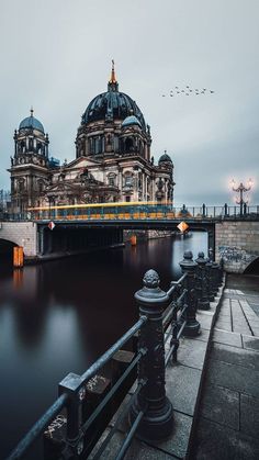 a large building sitting on the side of a river next to a bridge with birds flying over it