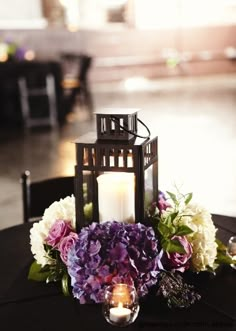 a candle and some flowers on a black table cloth with candles in the centerpiece