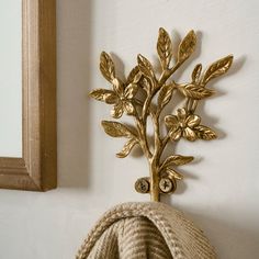 a gold leafy wall decoration on a white wall next to a beige towel and mirror