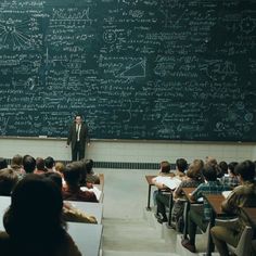 a man standing in front of a blackboard with lots of writing on it