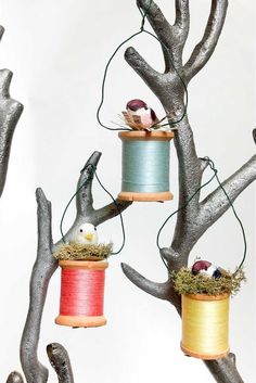 three spools of thread are hanging from tree branches with birds perched on them