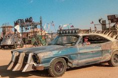 an old blue car parked in the dirt