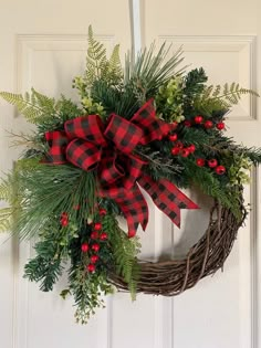 a wreath hanging on the front door with red and black plaid bow, evergreen leaves, berries and pine cones