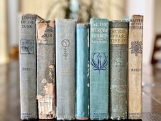 a row of old books sitting on top of a wooden table next to a vase